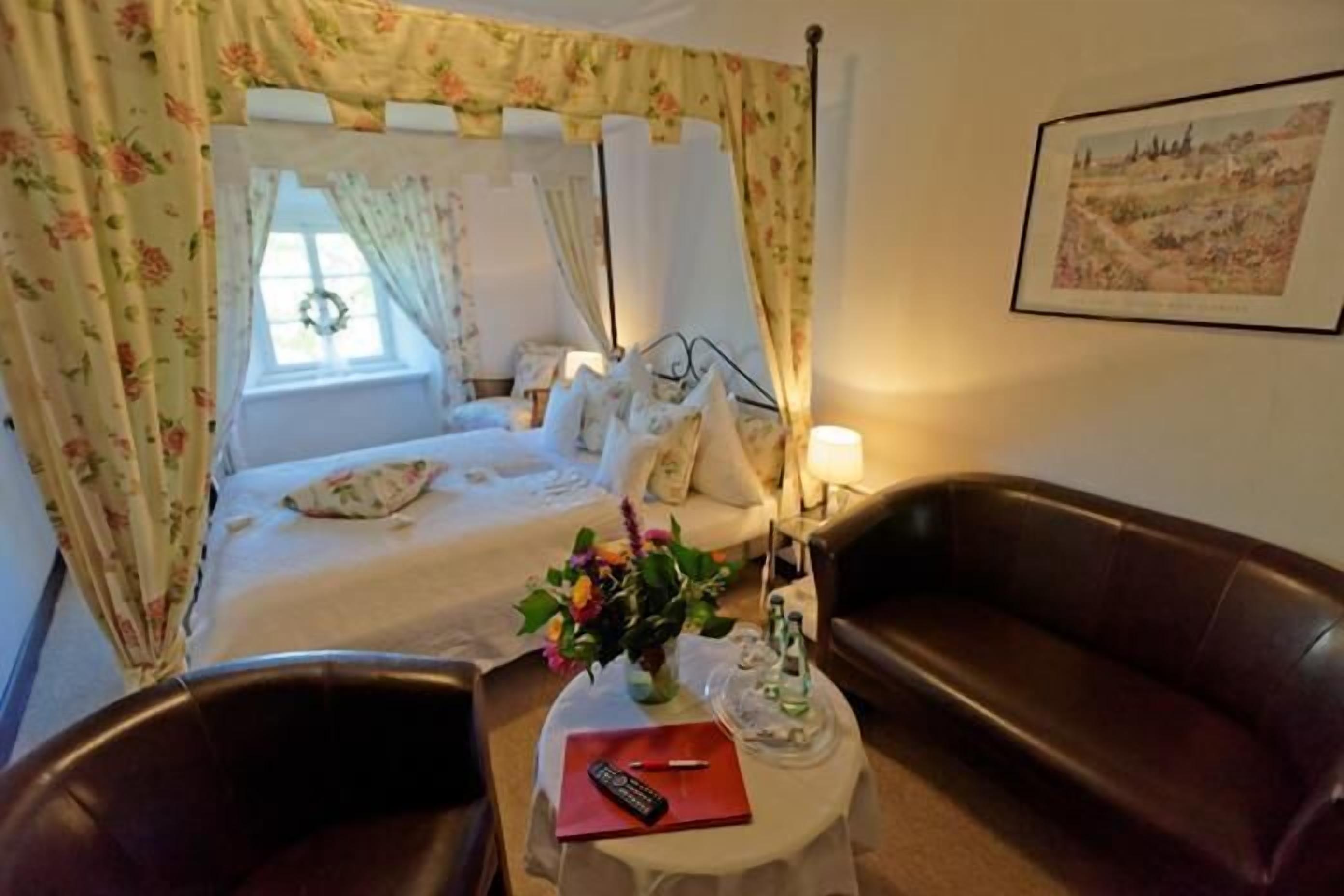 Un dormitorio con cama, mesita de noche, lámpara, un florero con flores y un cuadro en la pared.