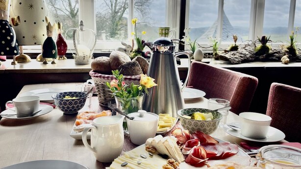 Una mesa de desayuno con diversos alimentos, una tetera y figuritas decorativas.