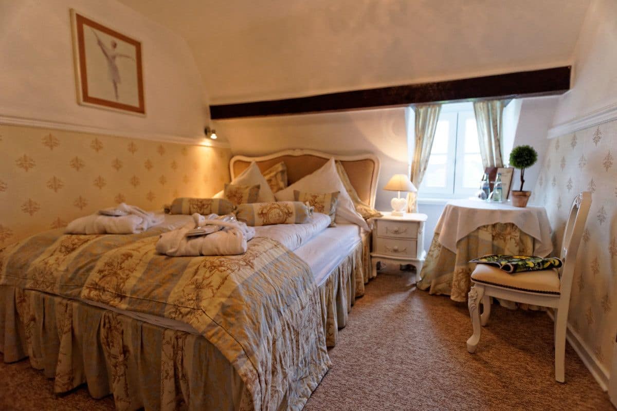 A bedroom with a large bed, a nightstand, a chair, and a small table with a lamp.