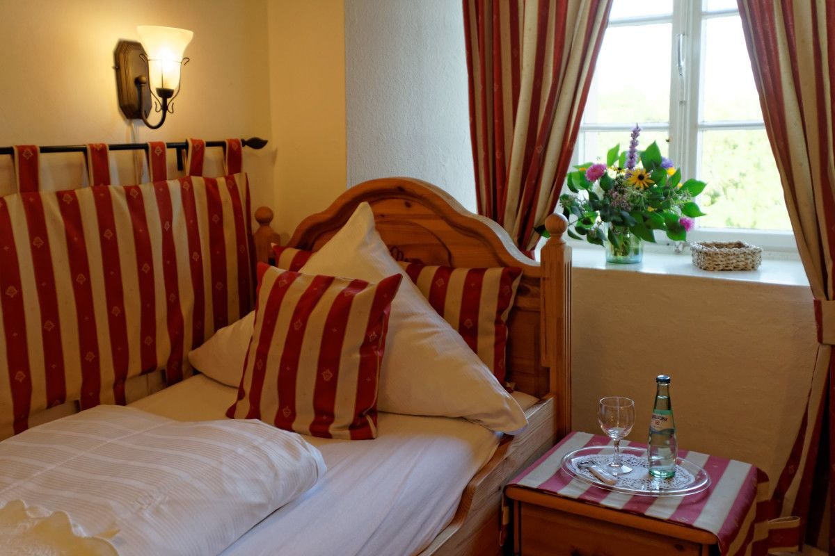 A hotel room with a bed, a bedside table with a bottle and glass, and a window with curtains.