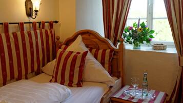 A hotel room with a bed, a bedside table with a bottle and glass, and a window with curtains.