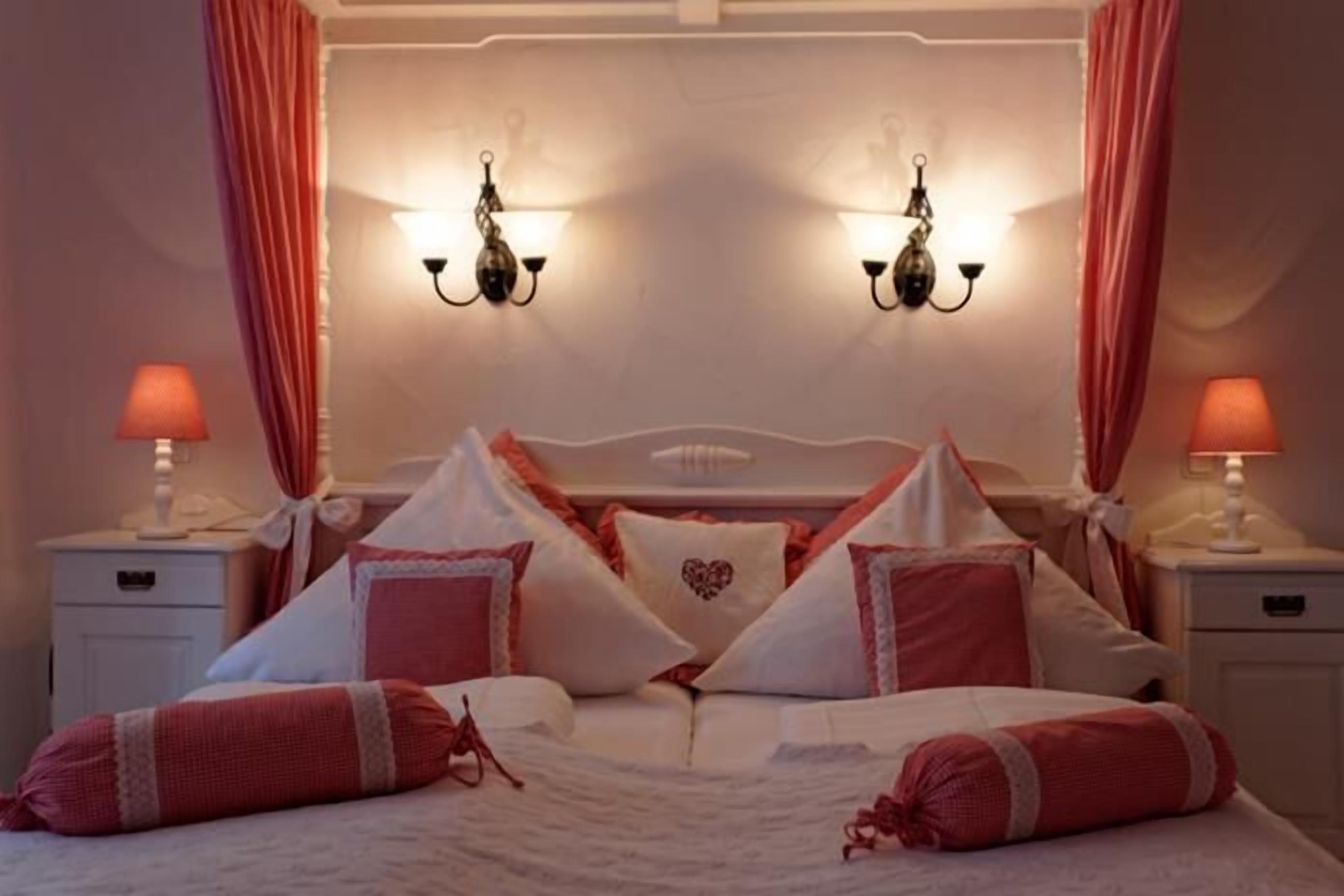 A neatly made bed with pink and white bedding, two wall-mounted lamps, and a nightstand with a lamp.