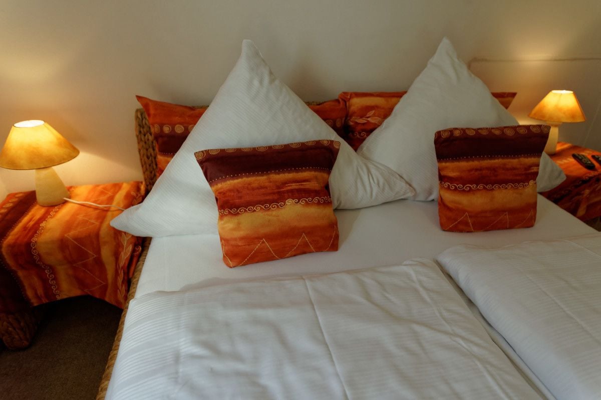A neatly made bed with white linens and decorative pillows, two bedside lamps, and a patterned bedspread.