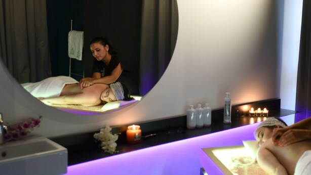A spa room with a massage table, a large mirror, and a shelf with candles and bottles. - Versomare (Polignano a Mare)