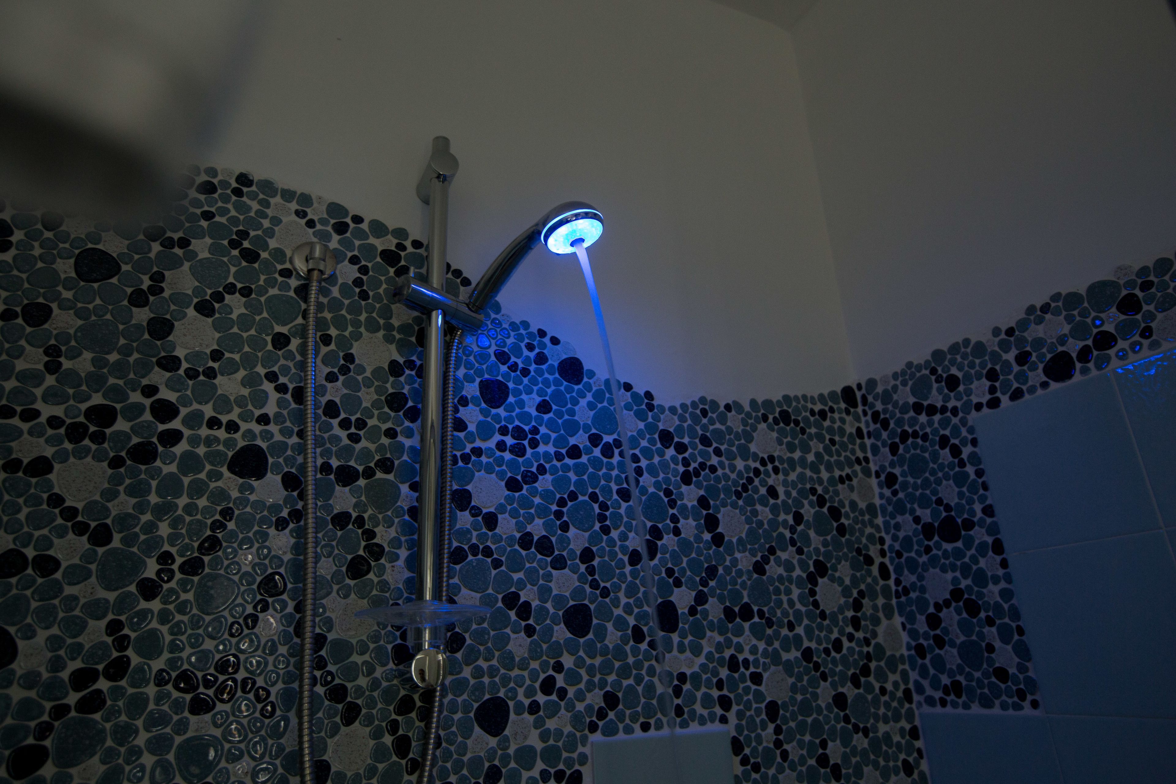 A shower with a blue-lit head, surrounded by a mosaic tile wall.