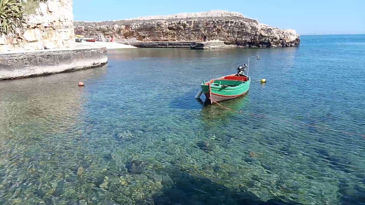 Un bote amarrado a un muelle, con agua cristalina y acantilados rocosos al fondo.