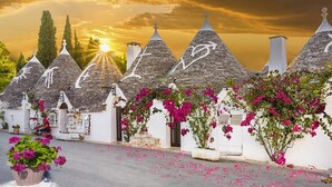 A row of traditional stone-roofed buildings with white walls and pink bougainvillea vines. - Versomare (Polignano a Mare)