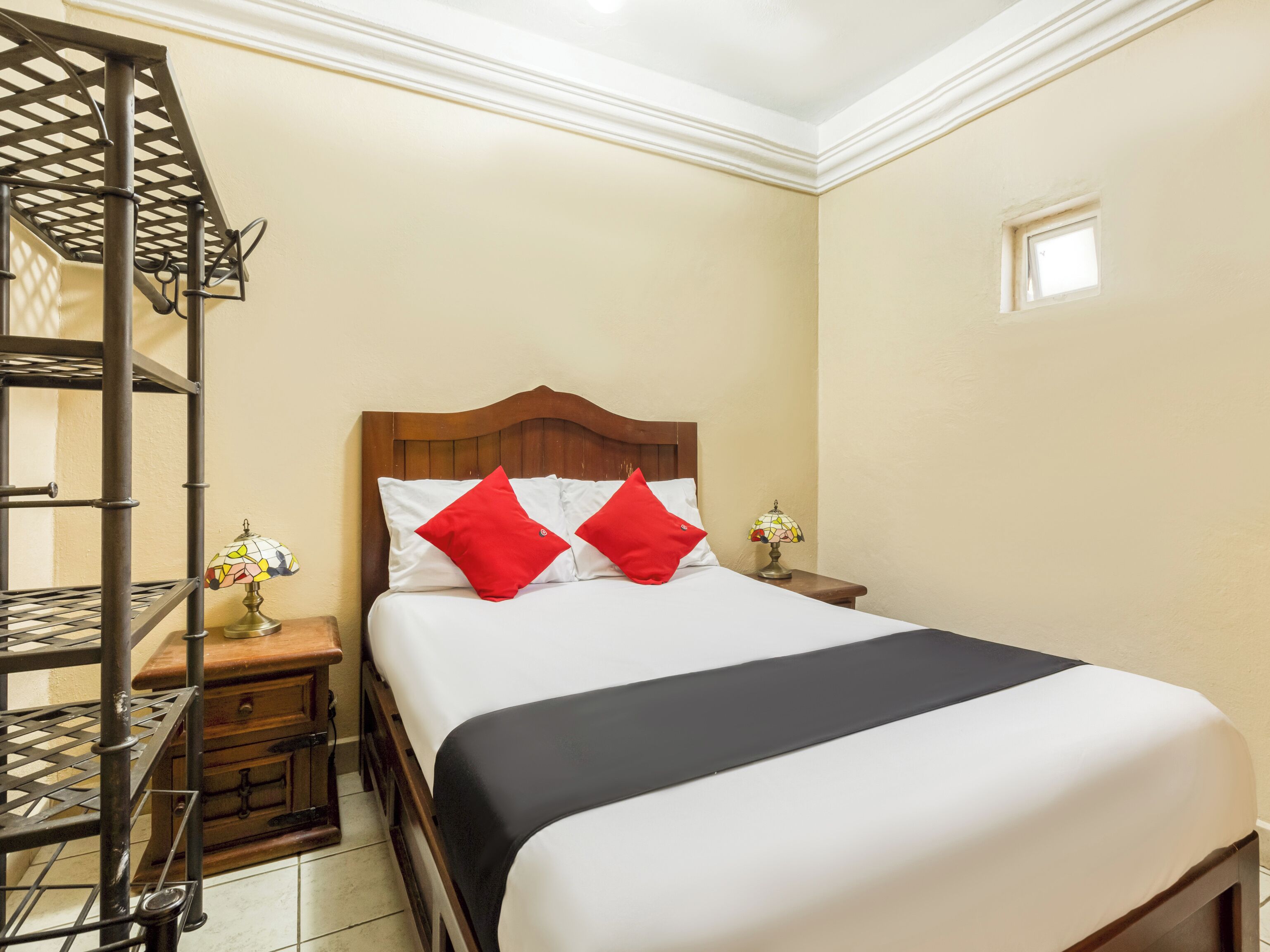 Habitación de hotel ordenada con cama, mesita de noche, lámpara y estante.