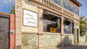Un edificio con un letrero que dice "Colina Dorada". Presenta fachada de piedra, ventanas grandes y un balcón con barandillas.