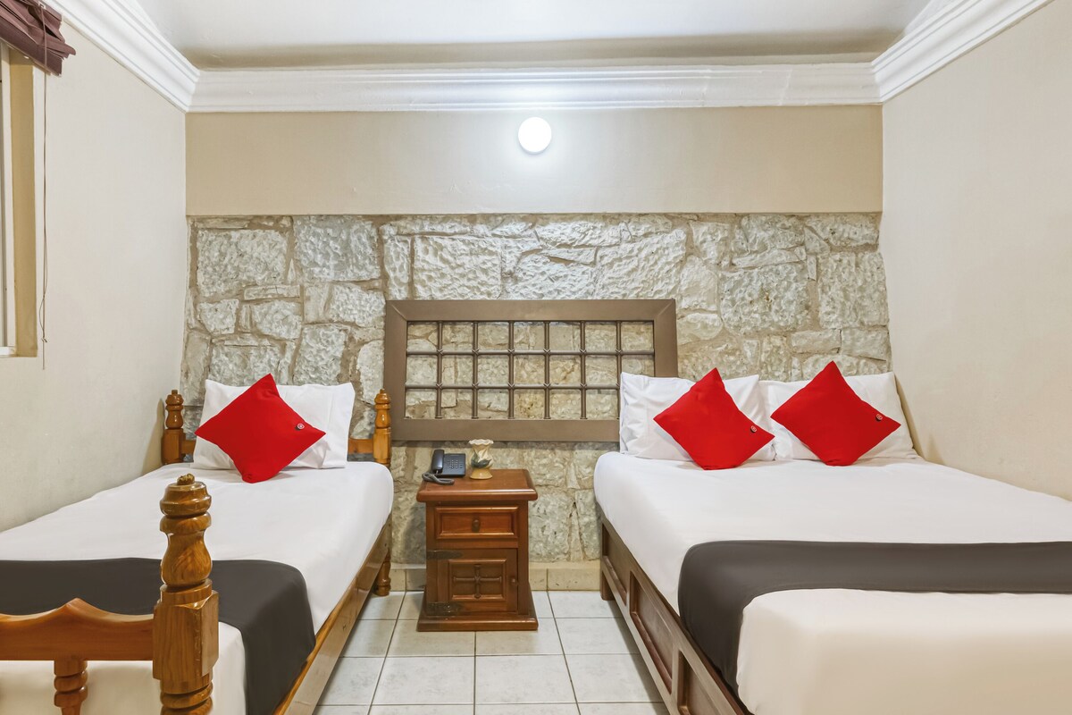 A room with two beds, a stone wall, a wooden headboard, a nightstand, and a telephone.