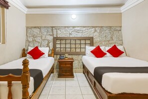 A hotel room with two beds, a stone wall, a nightstand with a phone, and a wooden headboard. - Capital O Colina Dorada (Oaxaca)