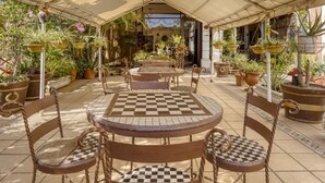 An outdoor patio with checkered tables and chairs, surrounded by potted plants and a covered area. - Capital O Colina Dorada (Oaxaca)