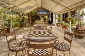 An outdoor patio with checkered tables and chairs, surrounded by potted plants and a covered area. - Capital O Colina Dorada (Oaxaca)