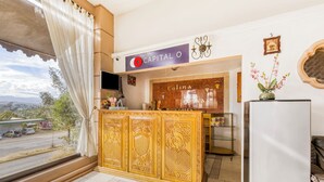 Zona de recepción de un hotel con un mostrador de madera, un cartel que dice "Capital O" y vistas al exterior.