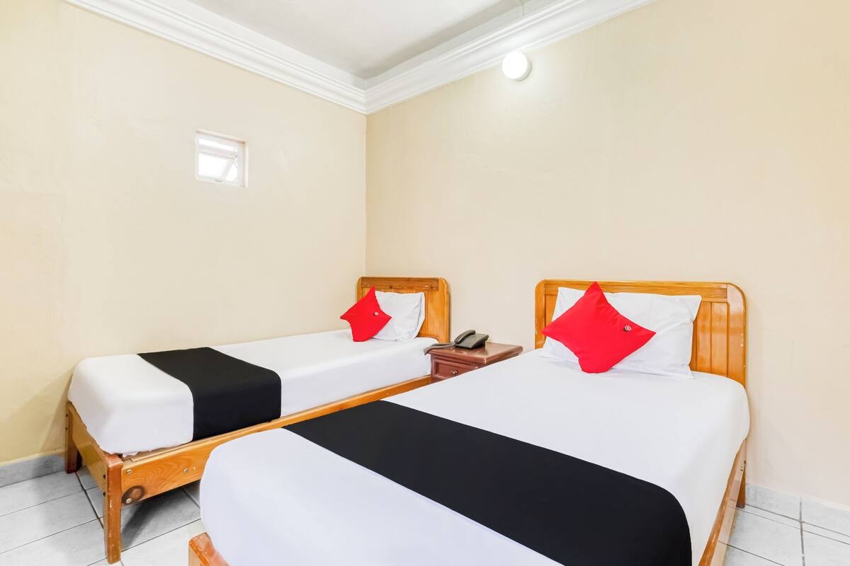 Hotellihuoneessa on kaksi erillistä sänkyä, joissa on molemmissa puinen pääty ja valkoiset vuodevaatteet sekä punaiset tyynyt. Huoneessa on myös pieni yöpöytä, jonka päällä on puhelin.