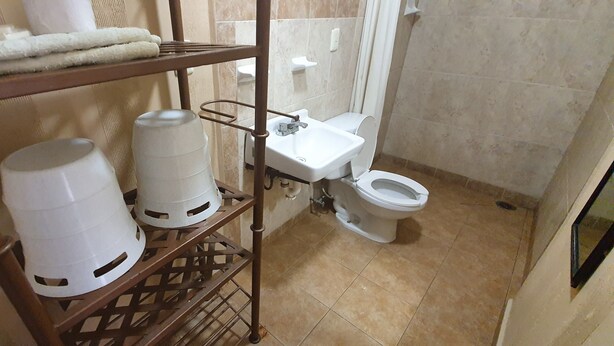 A bathroom with a toilet, a sink, and a shelf holding white containers. - Capital O Colina Dorada (Oaxaca)