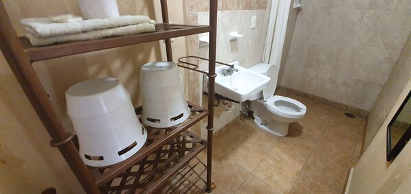 A bathroom with a toilet, a sink, and a shelf holding white containers. - Capital O Colina Dorada (Oaxaca)