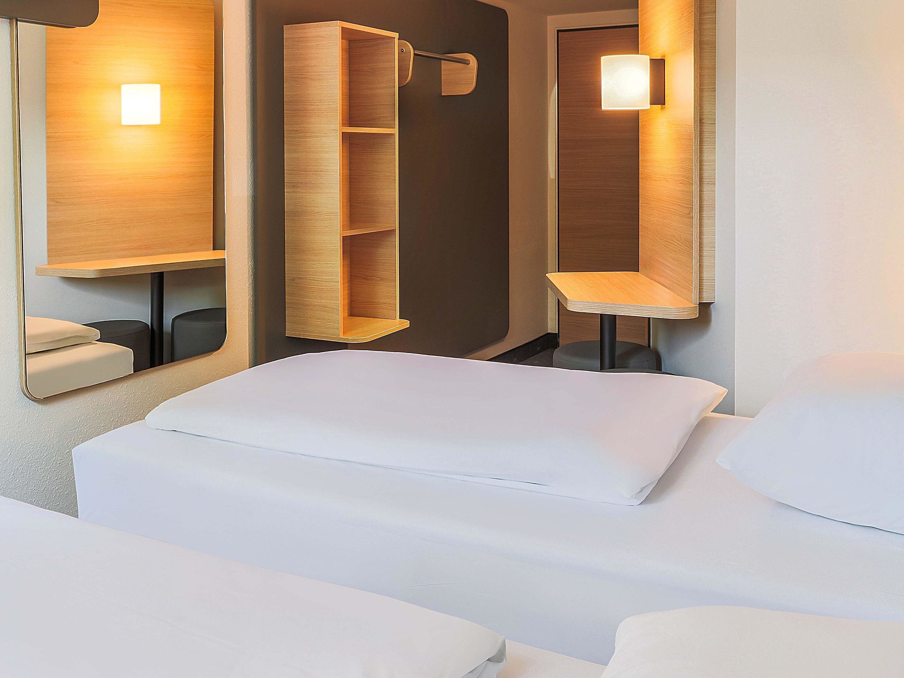 A hotel room with a bed, a wooden shelf unit, and a mirror with integrated lighting.