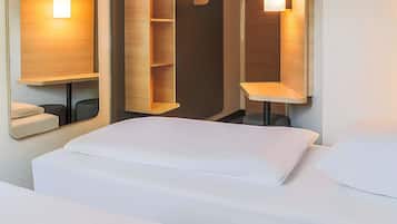 A hotel room with a bed, a wooden shelf unit, and a mirror with integrated lighting.