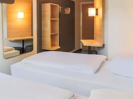 Habitación de hotel con cama, estantería de madera y espejo con iluminación integrada.