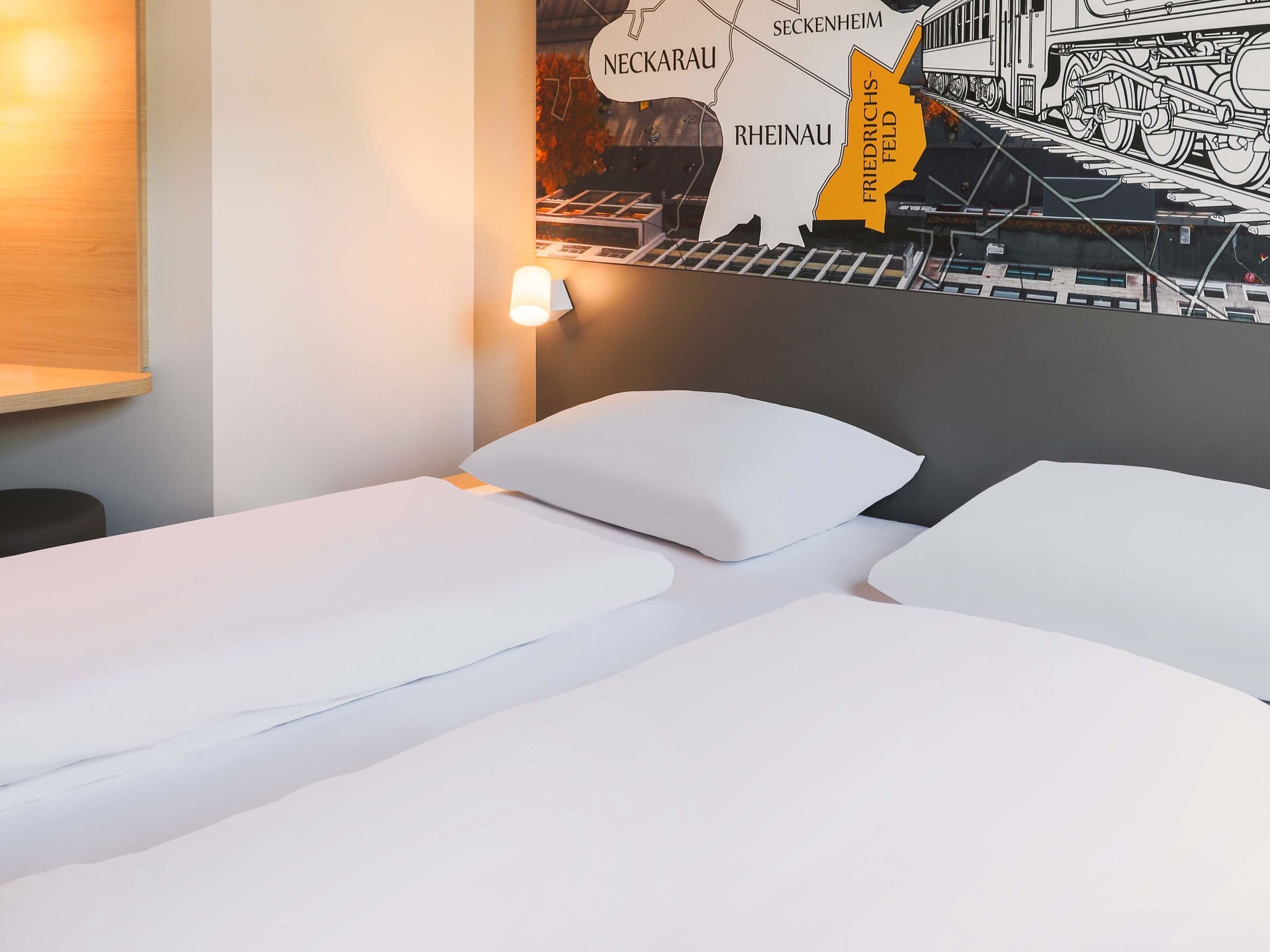 A hotel room with a bed, pillows, a wall-mounted light, and a map of Germany.