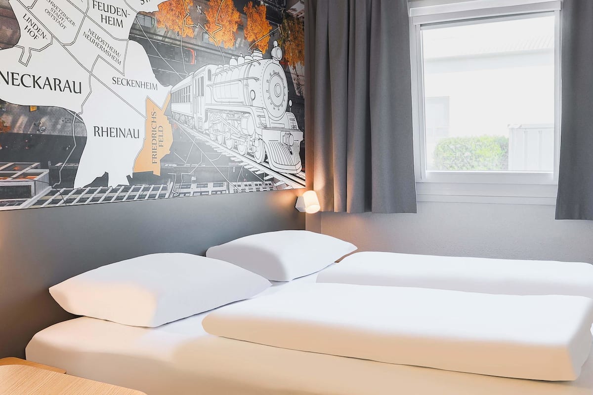 Une chambre d’hôtel avec deux lits, une table en bois et une fresque murale représentant un train.