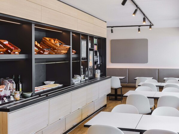 A modern restaurant with a long counter, white chairs, and a large screen on the wall.