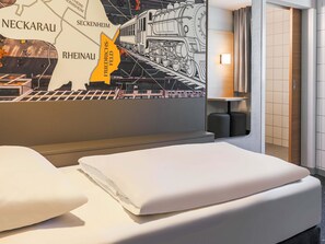 Une chambre d’hôtel avec un lit, une carte accrochée au mur et une lampe.