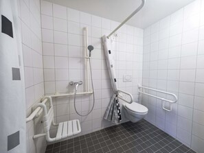A wheelchair-accessible bathroom with a white toilet, a shower with a grab bar, and a safety rail. - B&B HOTEL Leipzig-Schönefeld (Leipzig)