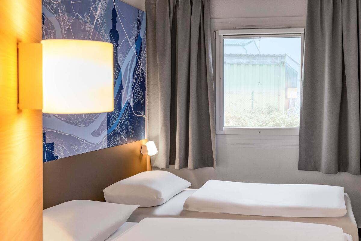 A hotel room with two beds, a large window, and a wall with a map design.