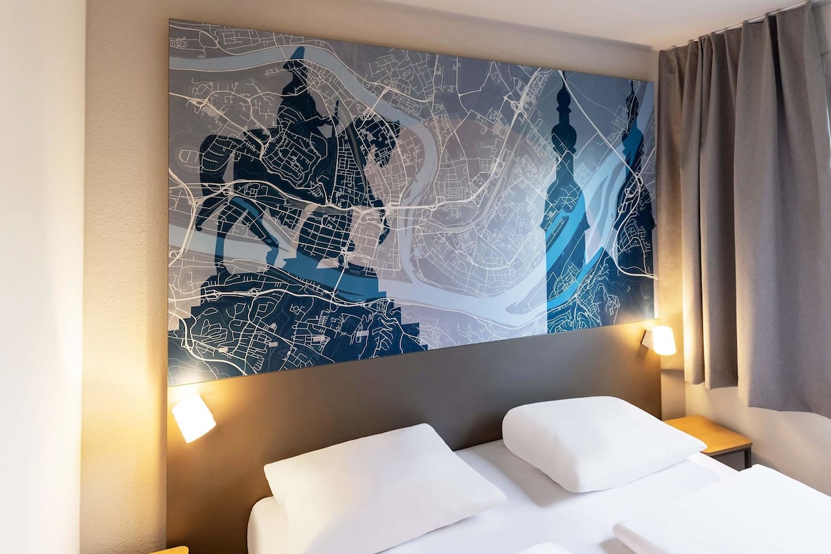 A hotel room with a large abstract painting on the wall, a bed with white linens, and two bedside lamps.