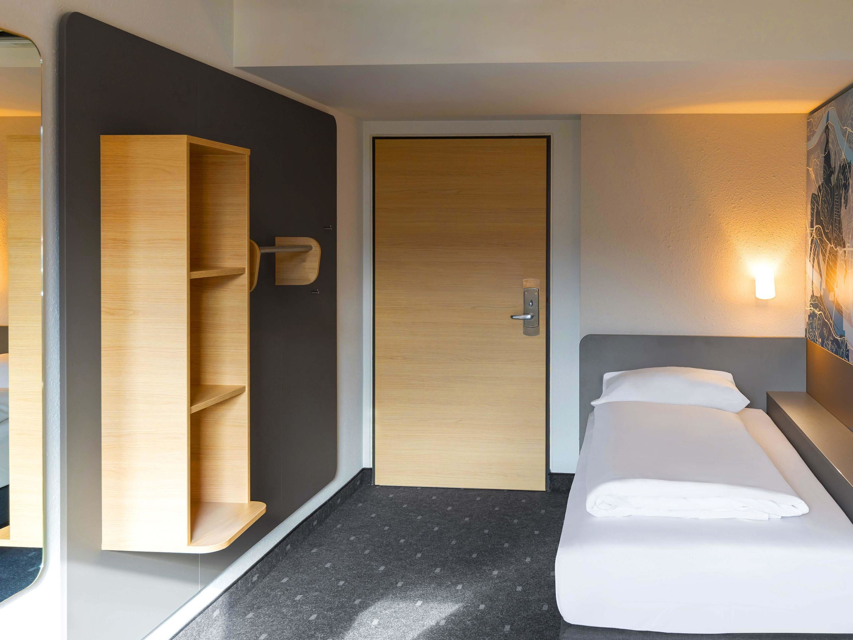 A hotel room with a bed, a wardrobe, a door, and a wall-mounted light fixture.