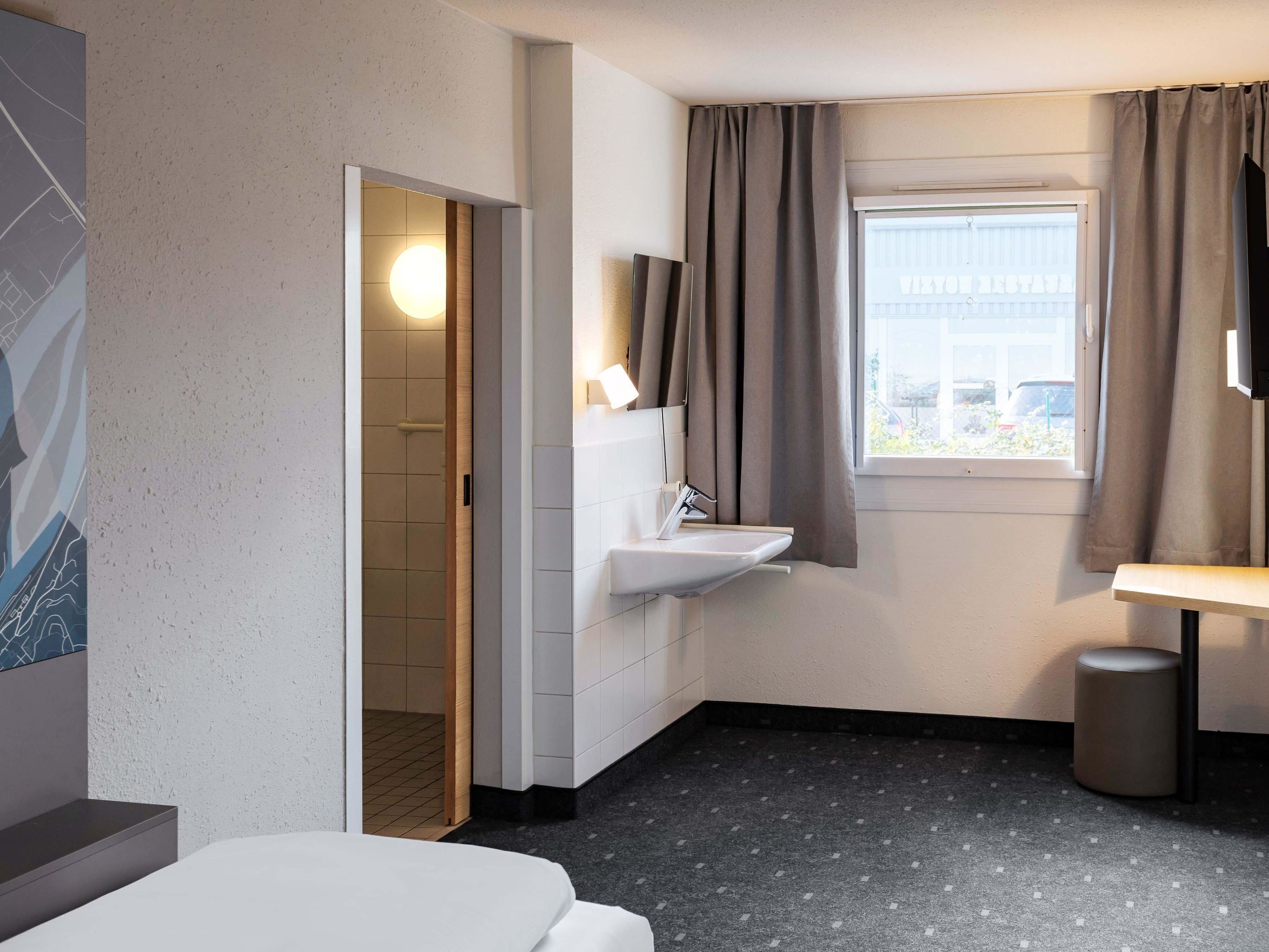 A hotel bathroom with a sink, mirror, and window.