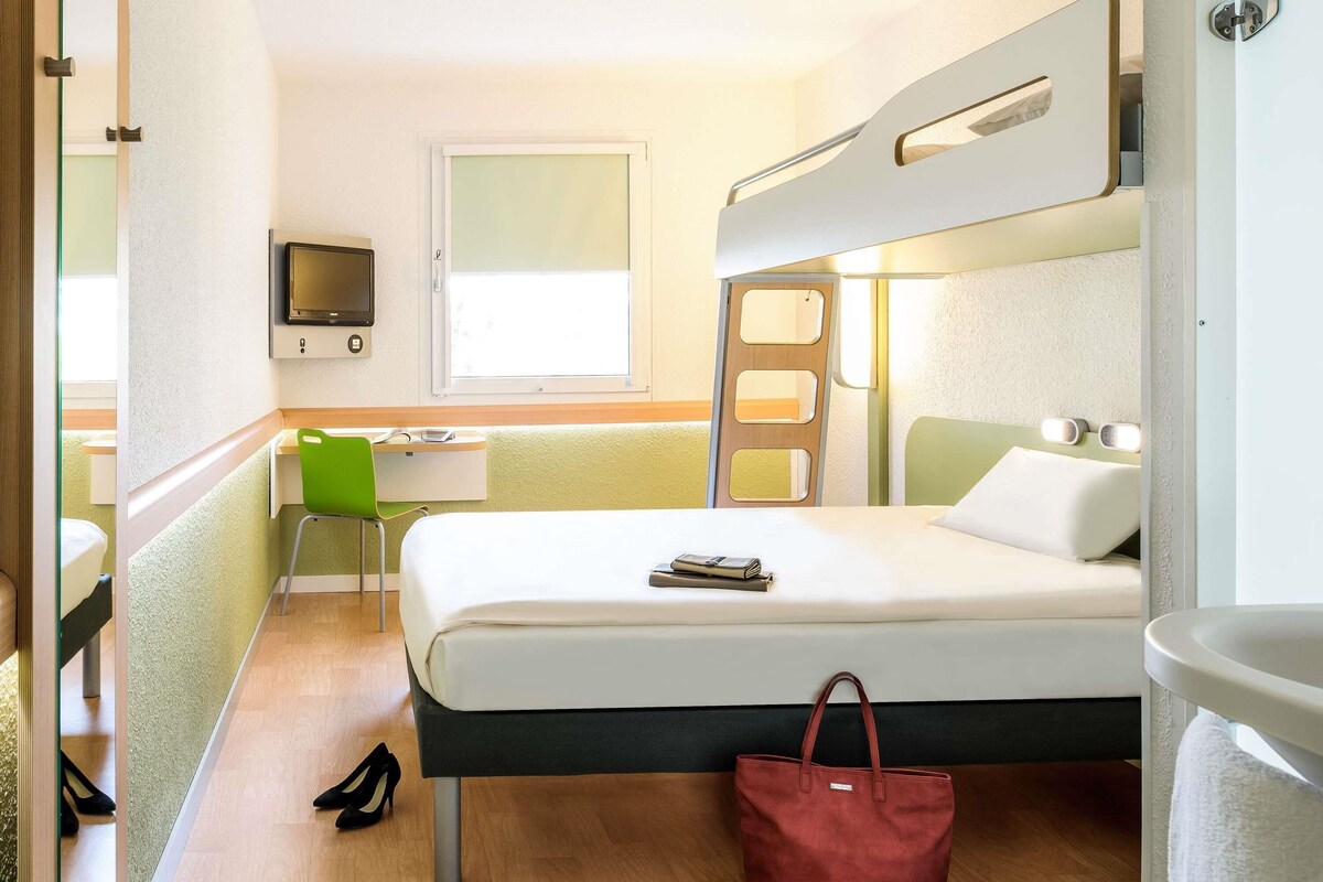 A hotel room with a bed, a desk, a chair, a TV, and a bathroom.