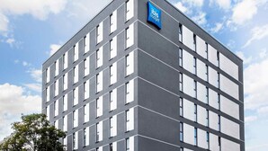 A modern building with a prominent 'ibis budget' sign, featuring a grid of windows and a flat roof.