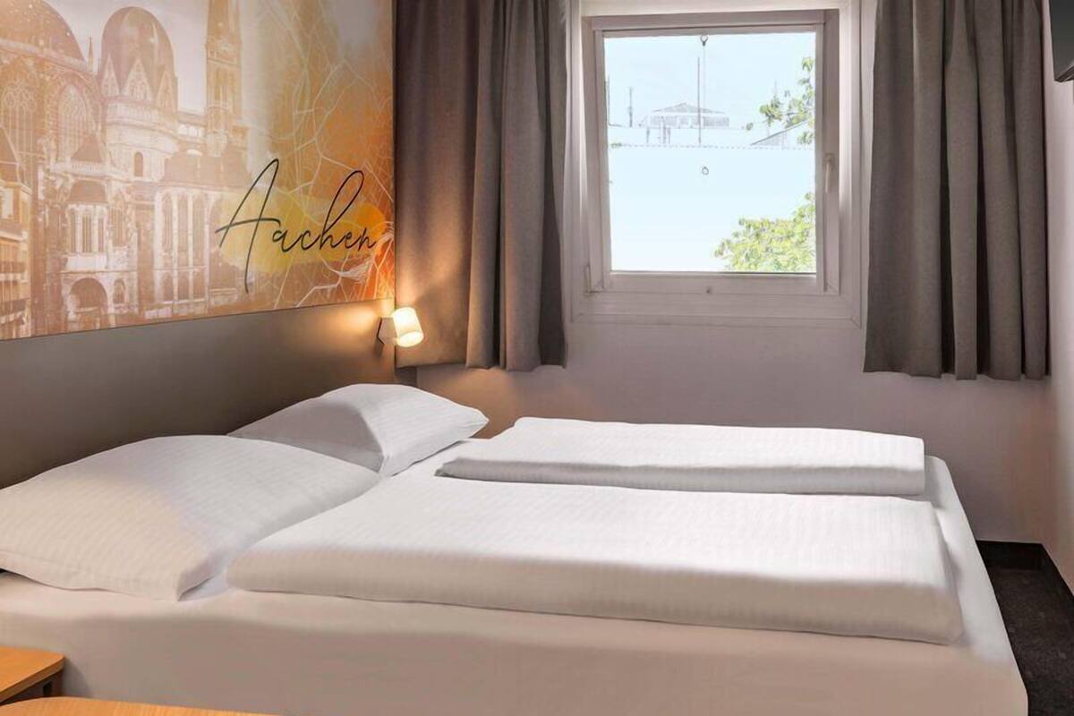 Hotelkamer met twee bedden, een nachtkastje, een raam met gordijnen en een muur met een stadsgezichtsmural.