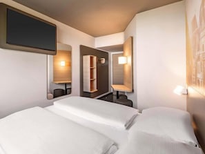 Une chambre d’hôtel équipée d’un lit, d’une télévision, d’un miroir et d’une étagère fixée au mur.