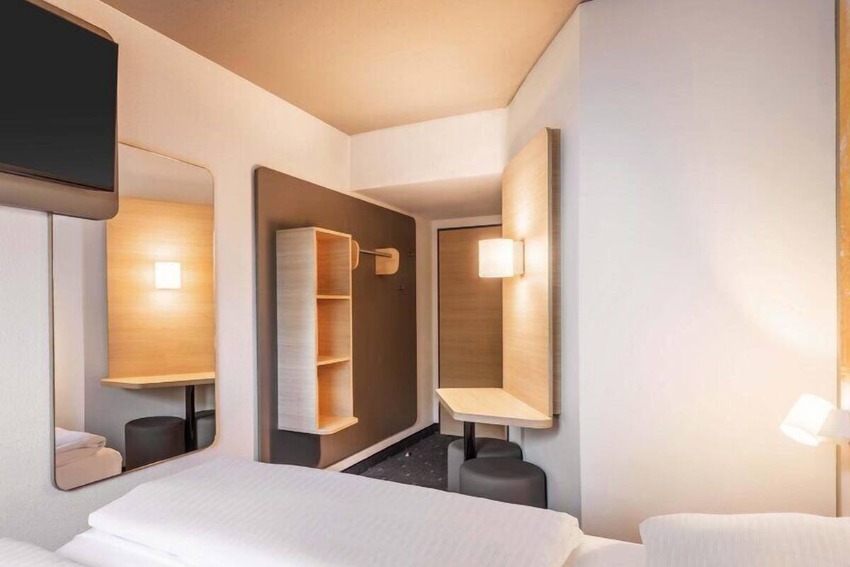 Een hotelkamer met een bed, een spiegel, een nachtkastje, een lamp en een kledingkast.