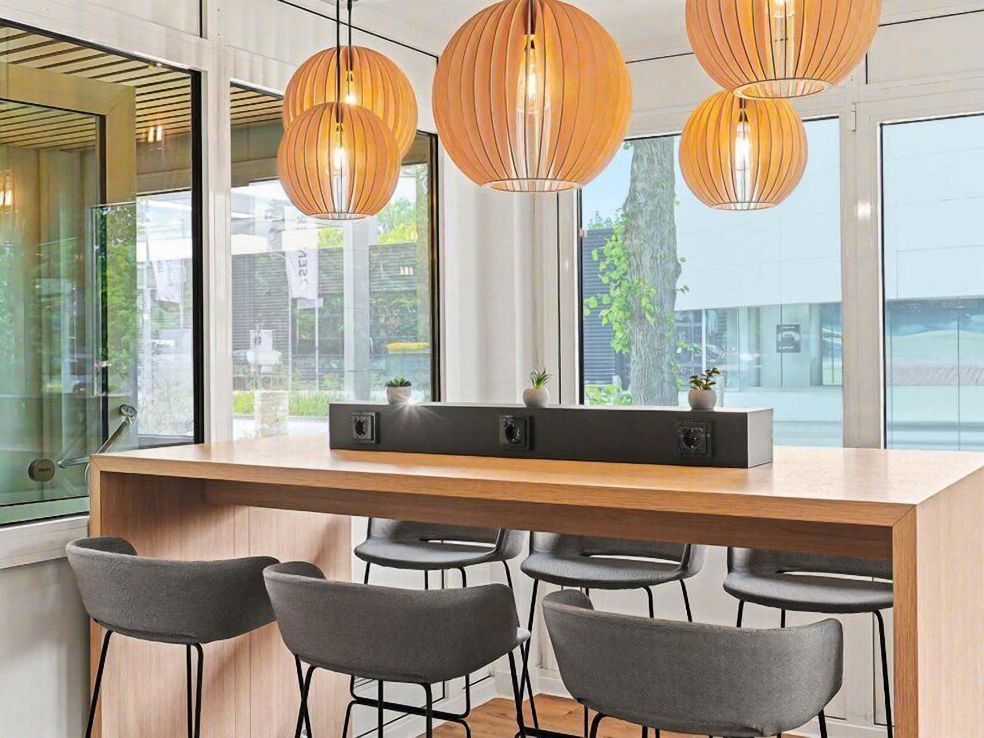 Eine moderne Bar mit einer langen Theke, vier Barhocker und drei Pendelleuchten.