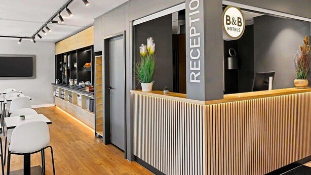 Un espace d’accueil avec un comptoir, des chaises, un téléviseur et un panneau indiquant « B&B Hotels ».