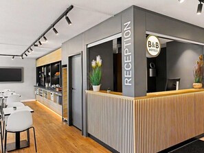 Een receptiegedeelte met een balie, stoelen, een televisie en een bordje voor B&B Hotels.