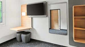 Une chambre d’hôtel moderne équipée d’un téléviseur à écran plat, d’une étagère en bois, d’un miroir et d’un petit coin salon.