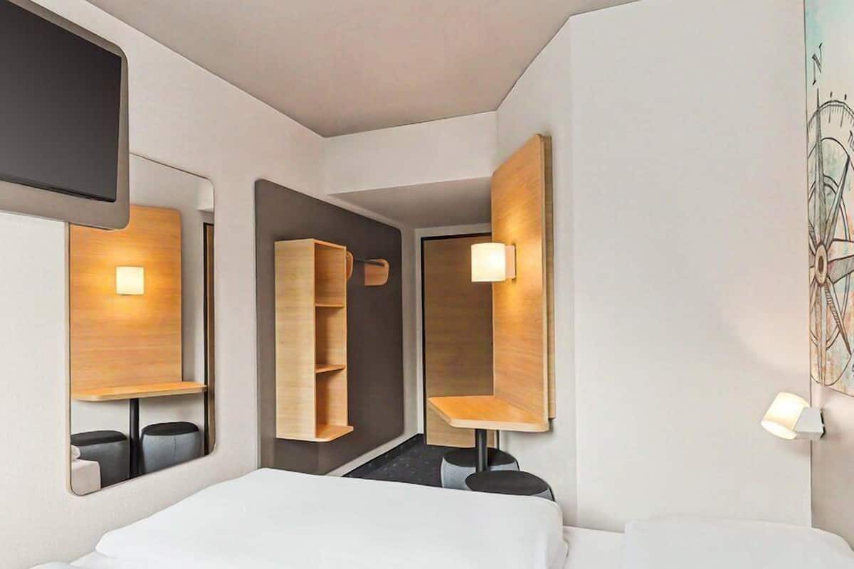 Une chambre d’hôtel équipée d’un lit, d’un miroir, d’une armoire et d’un téléviseur fixé au mur.