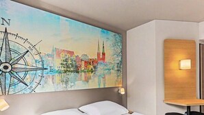Une chambre d’hôtel avec un lit, une œuvre d’art représentant une boussole fixée au mur, une table de chevet et une petite table à côté du lit.