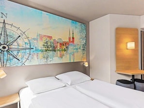 Une chambre d’hôtel avec un lit, une œuvre d’art représentant une boussole fixée au mur, une table de chevet et une petite table à côté du lit.
