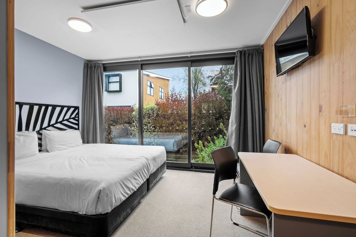 A modern hotel room with a bed, a desk, and a TV mounted on the wall.