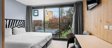 Quarto de hotel moderno com cama, escrivaninha e TV fixada na parede.