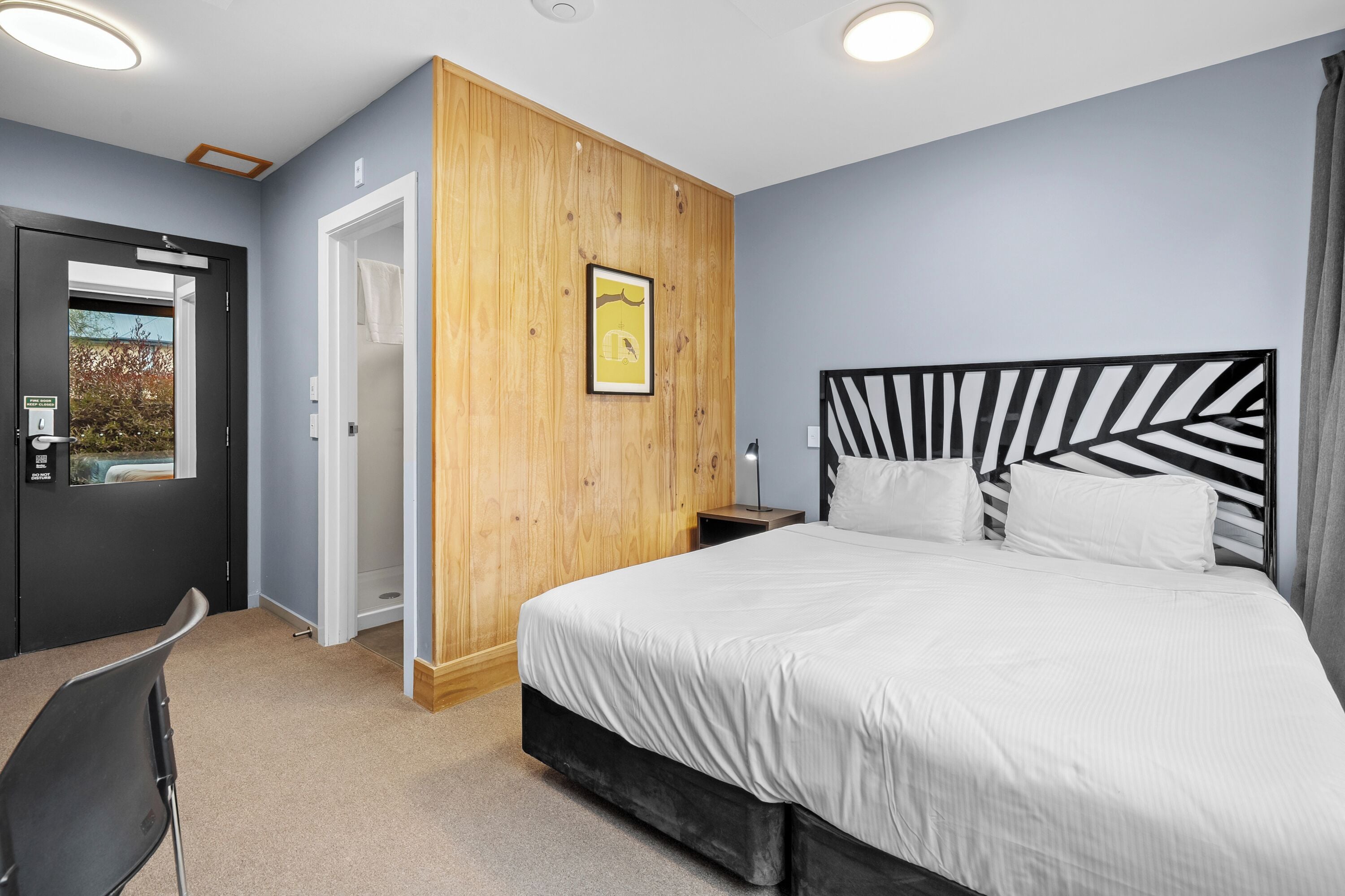 A bedroom with a bed, a wooden accent wall, a framed picture, and a door leading to a bathroom.