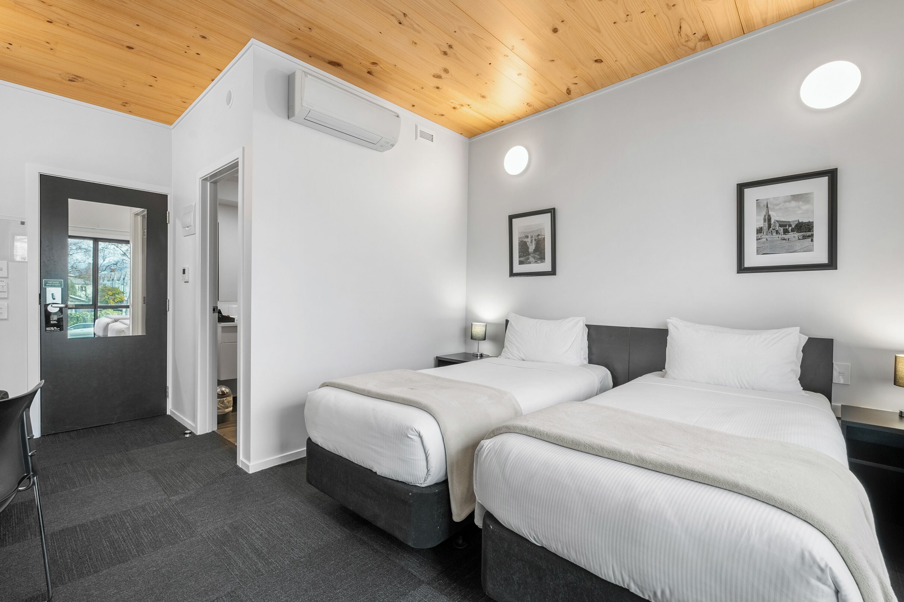 A hotel room with two beds, a desk, and a chair. There is a door leading to a balcony.