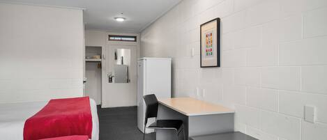 Habitación de hotel con dos camas, un escritorio, una silla, un refrigerador y un cuadro en la pared.